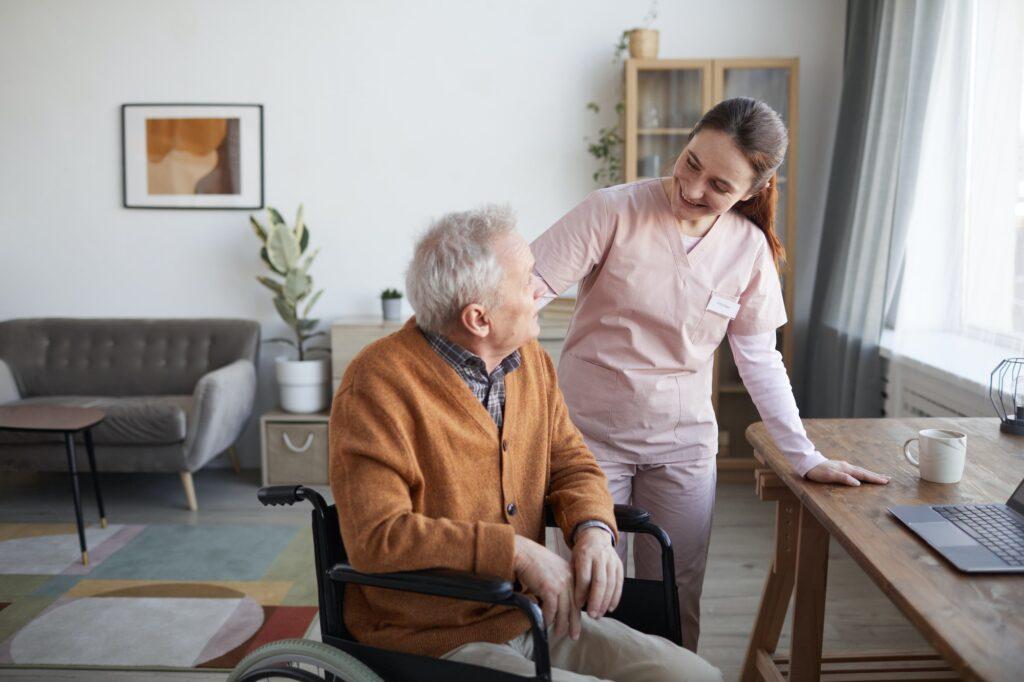 Smiling Young Woman Assisting Senior Man in Wheelchair